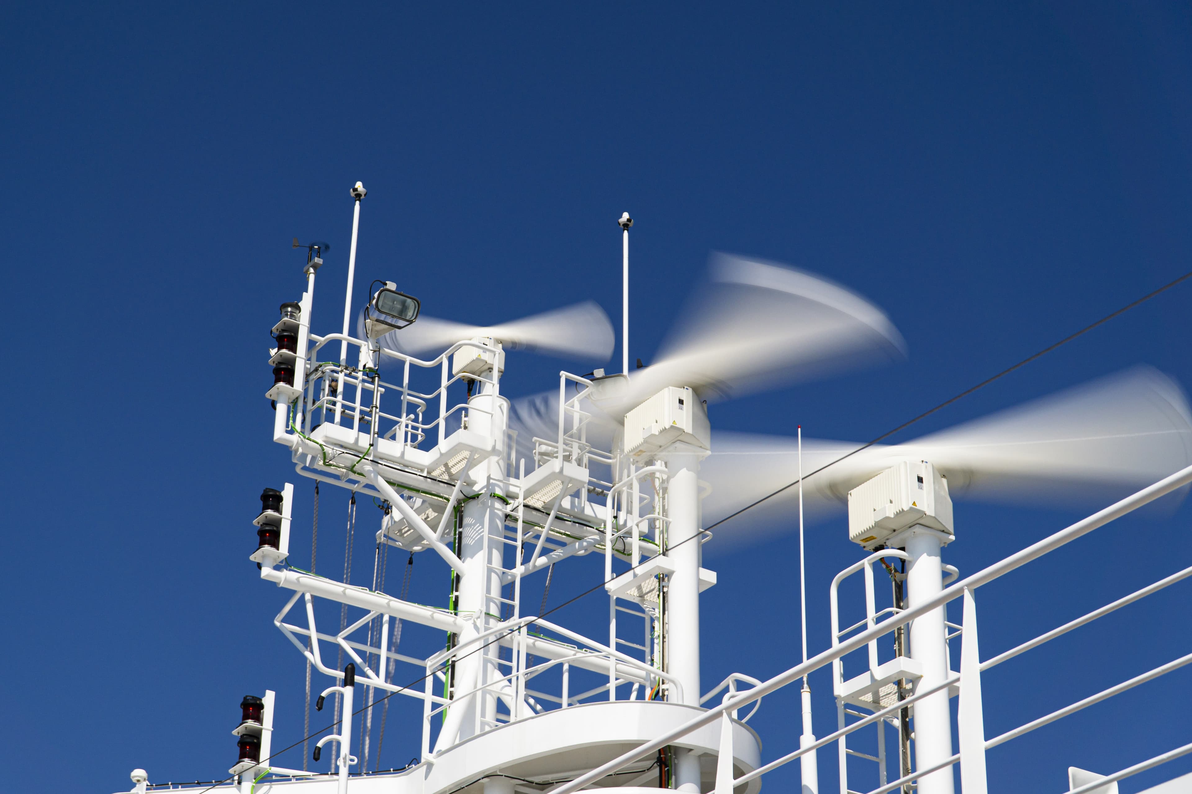 Rotating marine radar antennas aboard a vessel against a blue sky