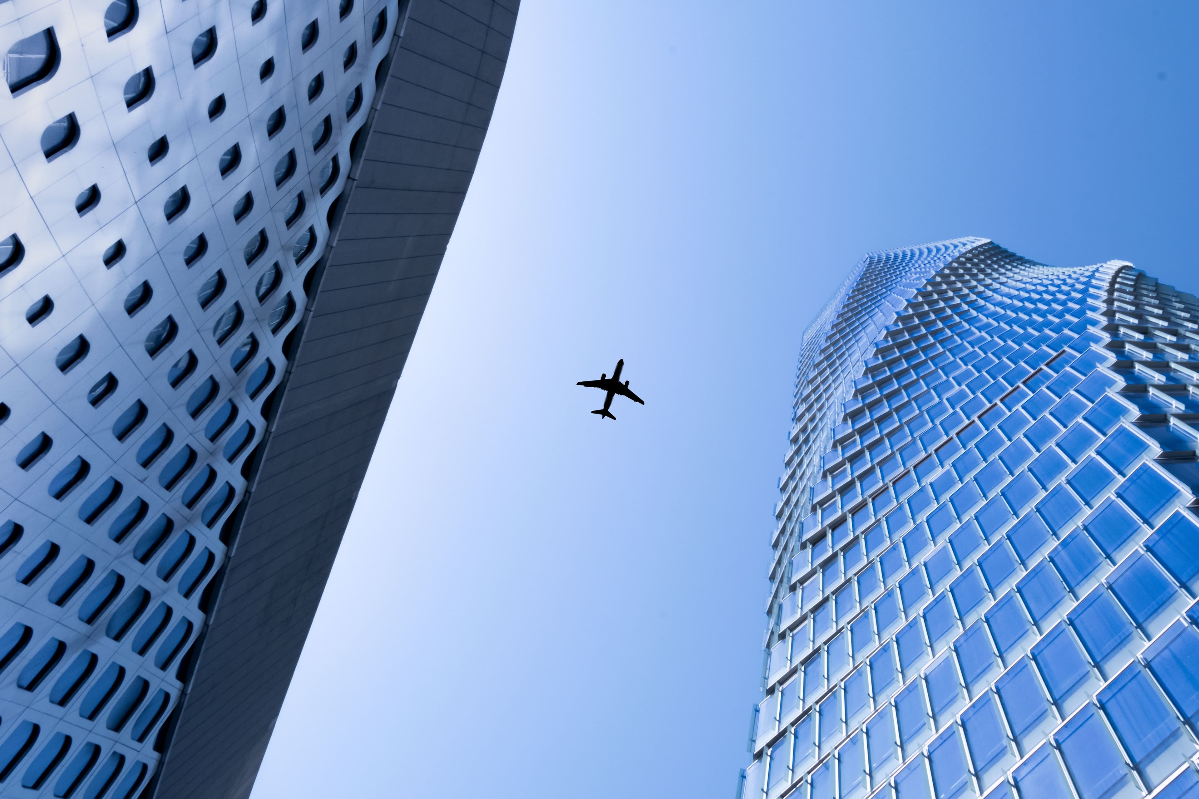Airplane flying between two modern buildings against a blue sky